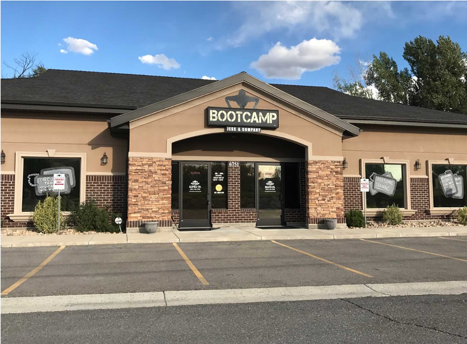 A single-story building with a sign reading "Bootcamp: Ink & Company" above the entrance, featuring brick and tan siding, large windows, and a small parking lot in front.